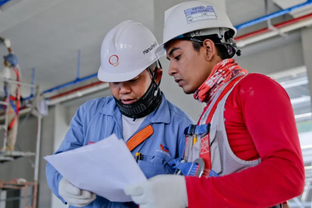 Two construction workers in safety gear reviewing documents at an indoor site.